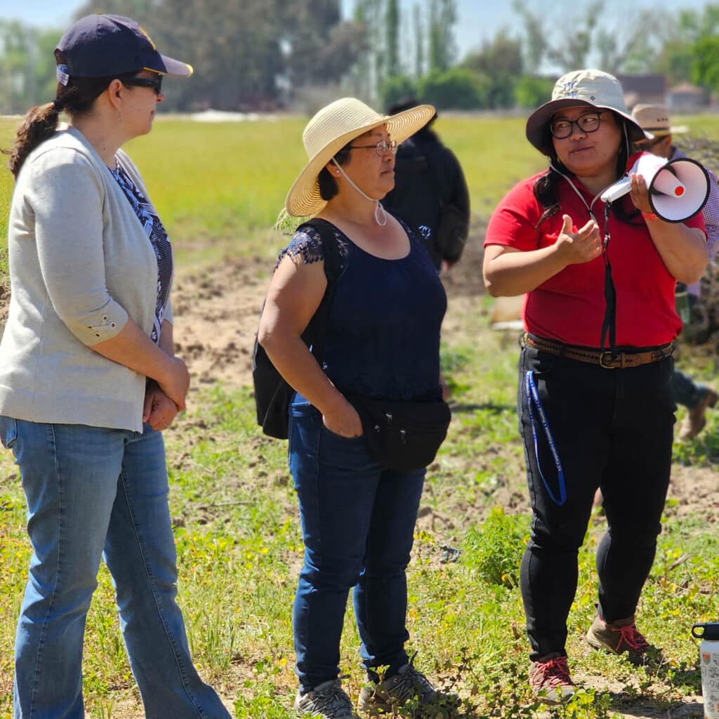 3 women speaking to visiting group on a farm